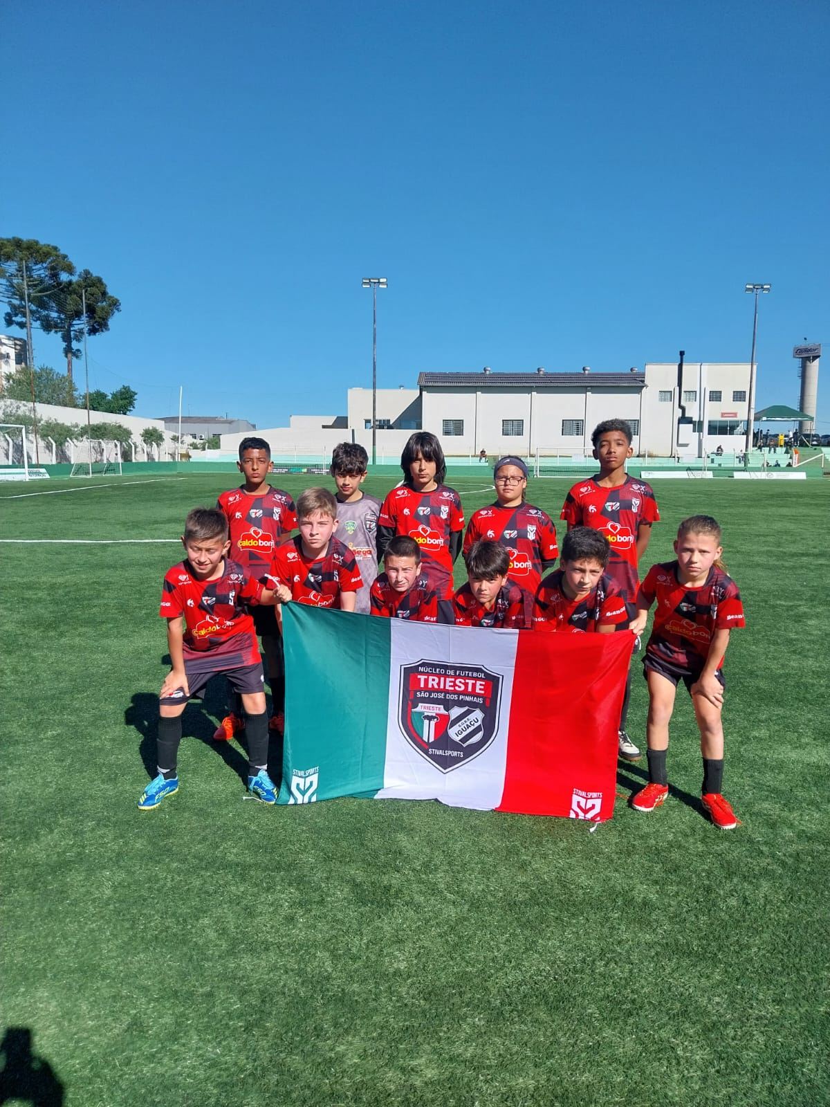 Equipe do Trieste em campo segurando a bandeira verde, branca e vermelha do clube
